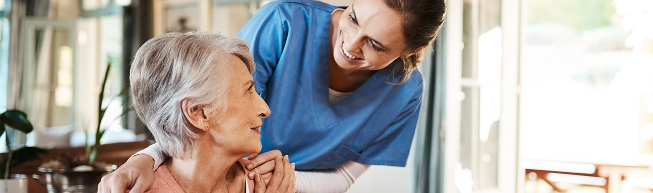 Pflegekraft serviert Seniorin Frühstück am Wohnzimmertisch und unterstützt sie freundlich im Alltag der ambulanten Pflege in Nettersheim.