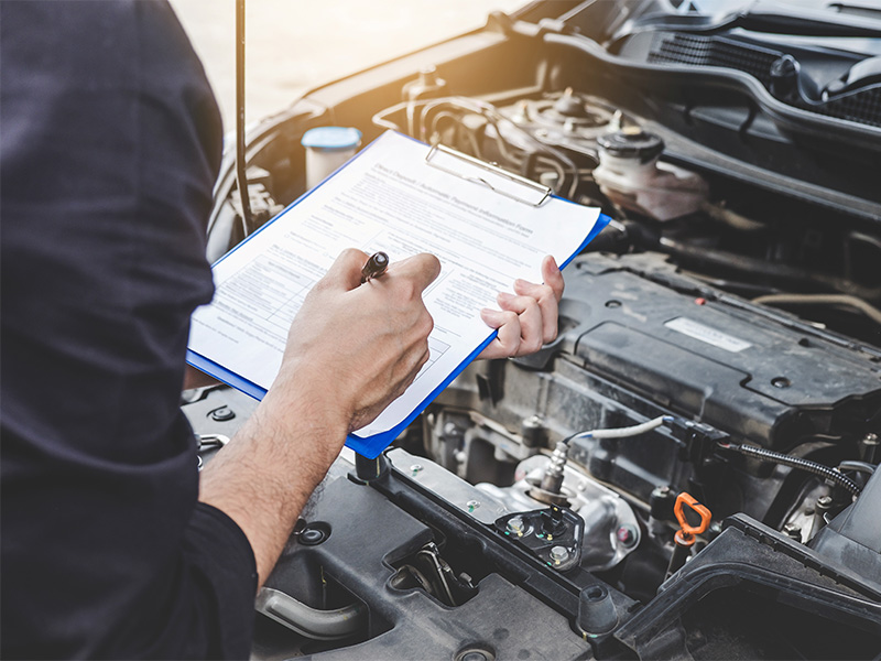Mechaniker führt Inspektion in Schleiden durch, prüft Motorraum sorgfältig und dokumentiert Ergebnisse auf einer Checkliste im Werkstattumfeld