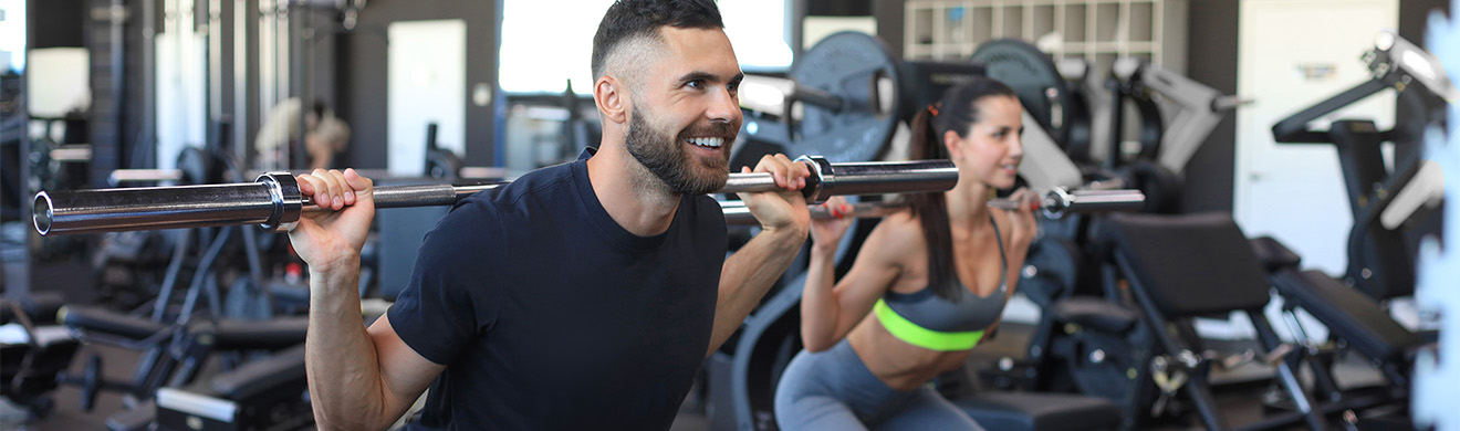 Durchtrainierter Mann und sportliche Frau heben Langhantel und zeigen Muskeln im modernen Fitnessstudio in Euskirchen