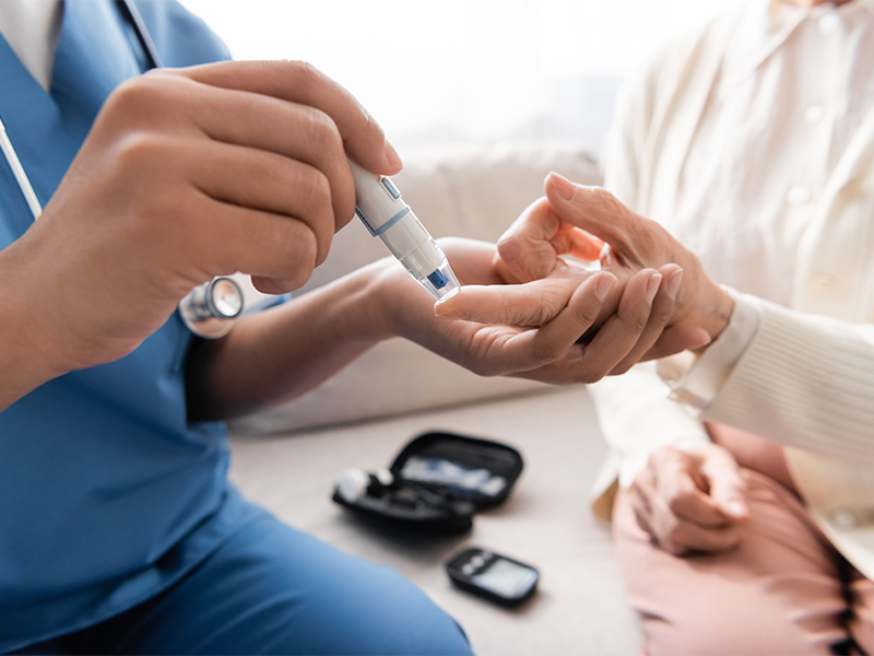 Pflegefachkraft entnimmt einer älteren Frau mit Lanzettenstift behutsam eine Blutprobe während Seniorenbetreuung in Mechernich zuhause.