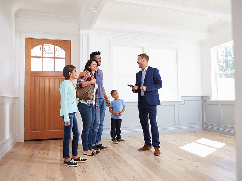 Makler in Euskirchen präsentiert einer Familie ein modernes Wohnhaus während einer professionellen Immobilienbesichtigung.