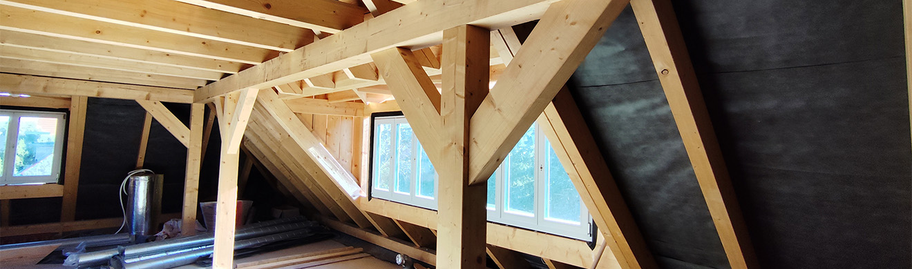 Dachgeschoss im Holzrahmenbau mit sichtbaren Holzbalken, Dachkonstruktion und moderner Wärmedämmung im Innenbereich.