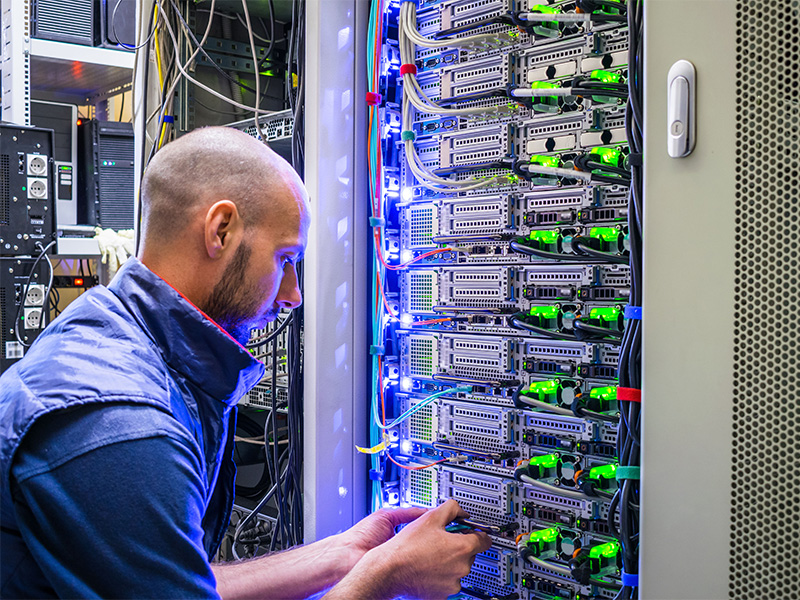 Techniker arbeitet im Serverraum an Routern und Netzwerkkabeln zur Absicherung moderner Cybersicherheit Infrastruktur