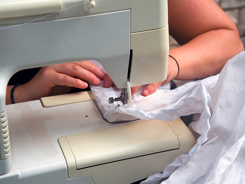 Frau näht helle Gardinen an Nähmaschine in gemütlichem Raum – Maßanfertigung für Gardinen nähen in Mechernich.