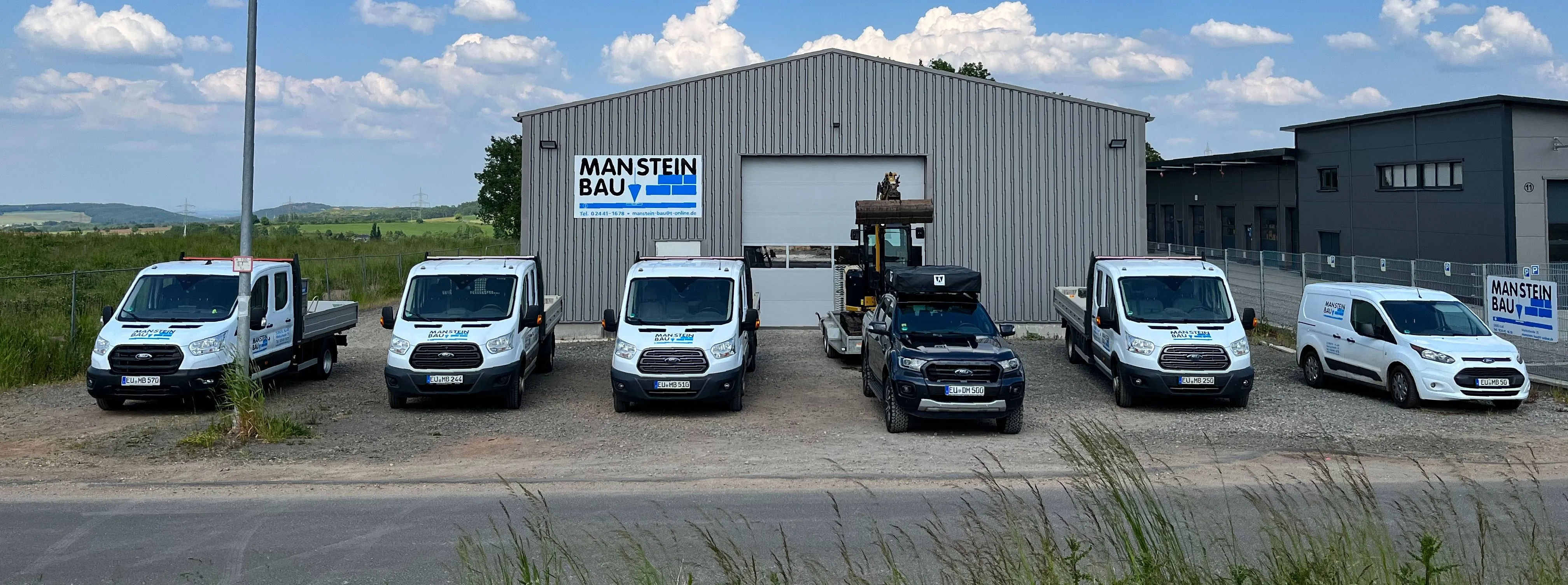 Firmengelände der Manstein Bau GmbH in Kall mit Firmengebäude, Baustellenfahrzeugen und moderner Ausstattung für professionelle Maurerarbeiten.