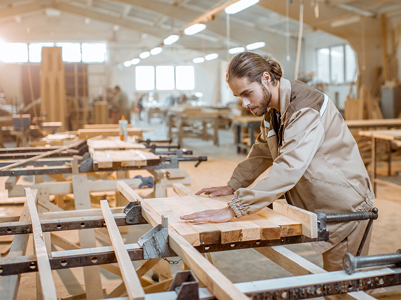 Schreiner in Arbeitskleidung verbindet Holzleisten in Werkstatt mit Holzleim und handwerklicher Präzision