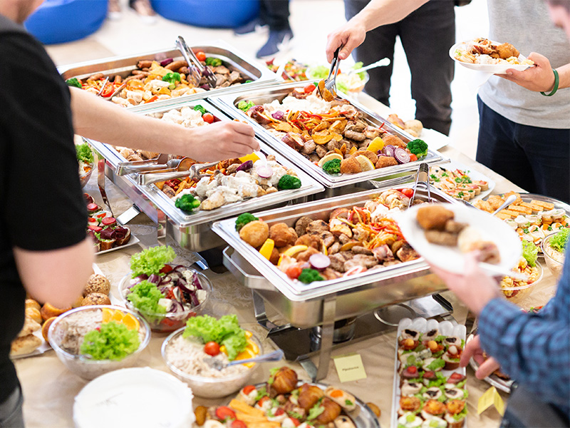 Hände von Gästen nehmen Speisen vom Buffet bei Veranstaltung mit professionellem Catering in Weilerswist und vielfältiger Auswahl.