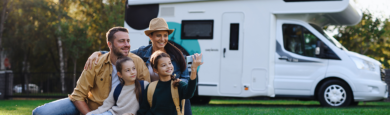 Gl&uuml;ckliche junge Familie mit zwei Kindern macht Selfie vor Wohnwagen im Freien bei Reisevorbereitung Campingplatz