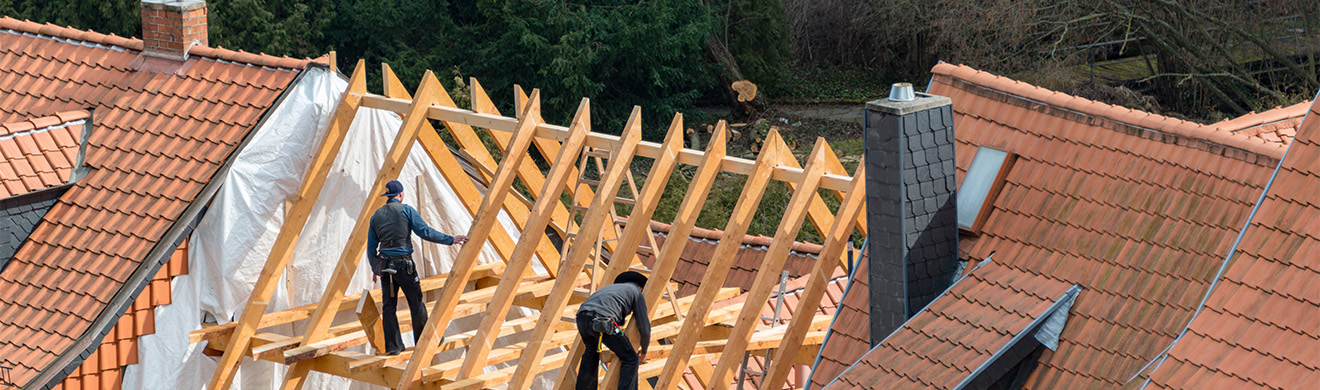 Zimmerleute und Dachdecker arbeiten gemeinsam an Dachstuhlarbeiten bei der Renovierung eines Holz-Dachstuhls auf einer Baustelle.